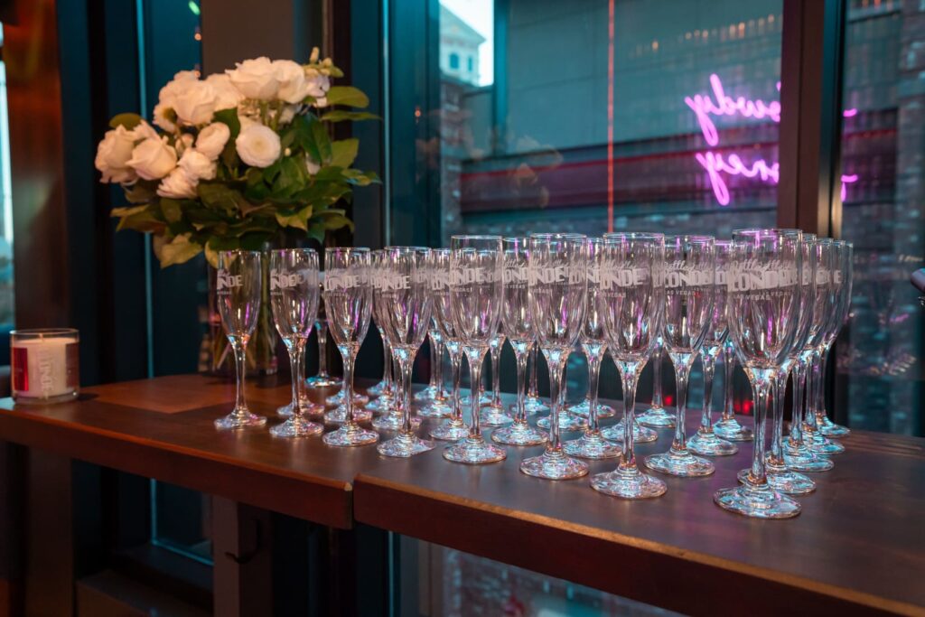 Bottled Blonde champagne flutes arranged beside a vase of white roses
