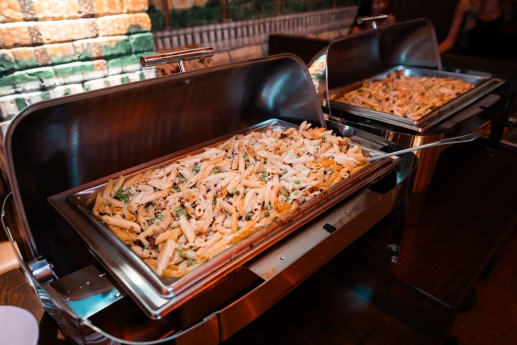 Buffet trays filled with creamy pasta and vegetables at the event