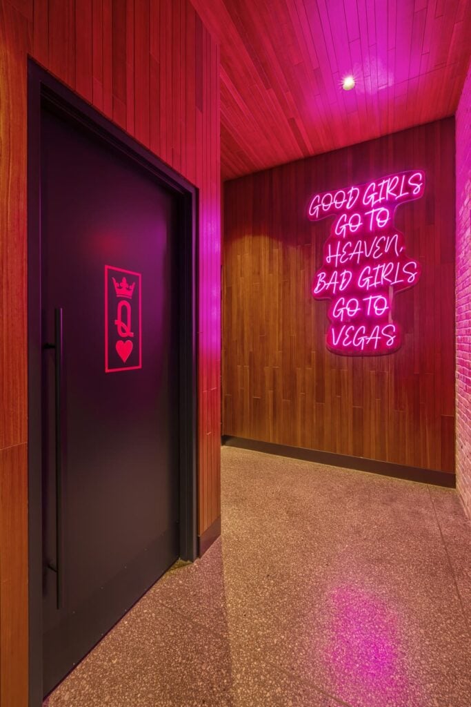 Neon pink sign on wood paneled wall reading Good girls go to heaven bad girls go to Vegas