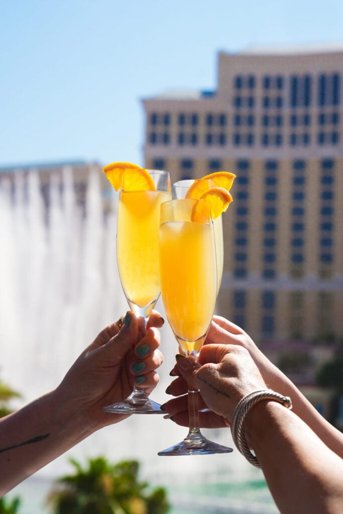 Three champagne flutes with orange slices held up in front of a hotel fountain