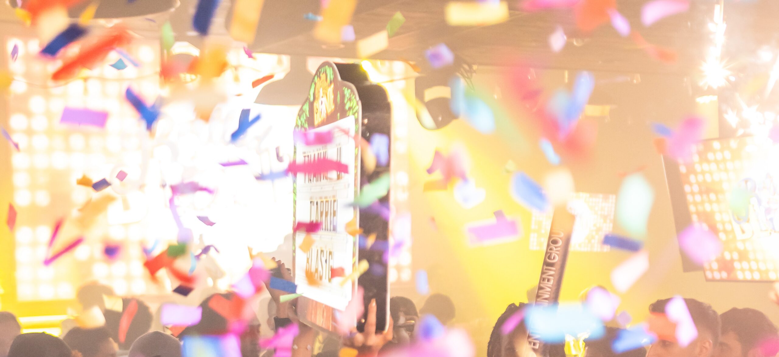 Bright nightclub scene filled with multicolored confetti and flashing lights, creating a vibrant party atmosphere with partially visible signs and energetic crowd.