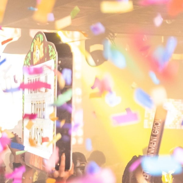 Bright nightclub scene filled with multicolored confetti and flashing lights, creating a vibrant party atmosphere with partially visible signs and energetic crowd.