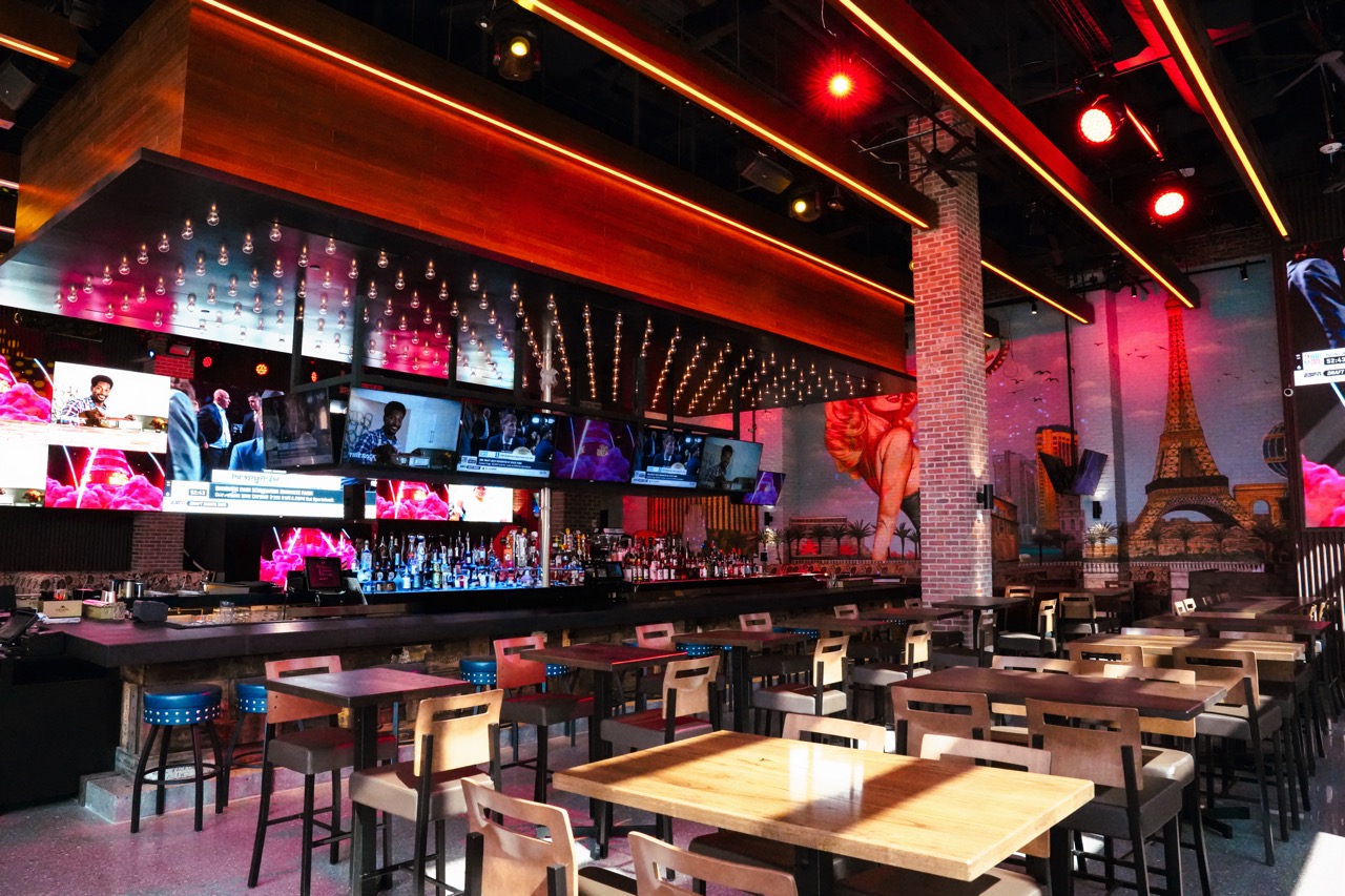 Bar and dining area with large mural and warm red ceiling lights.
