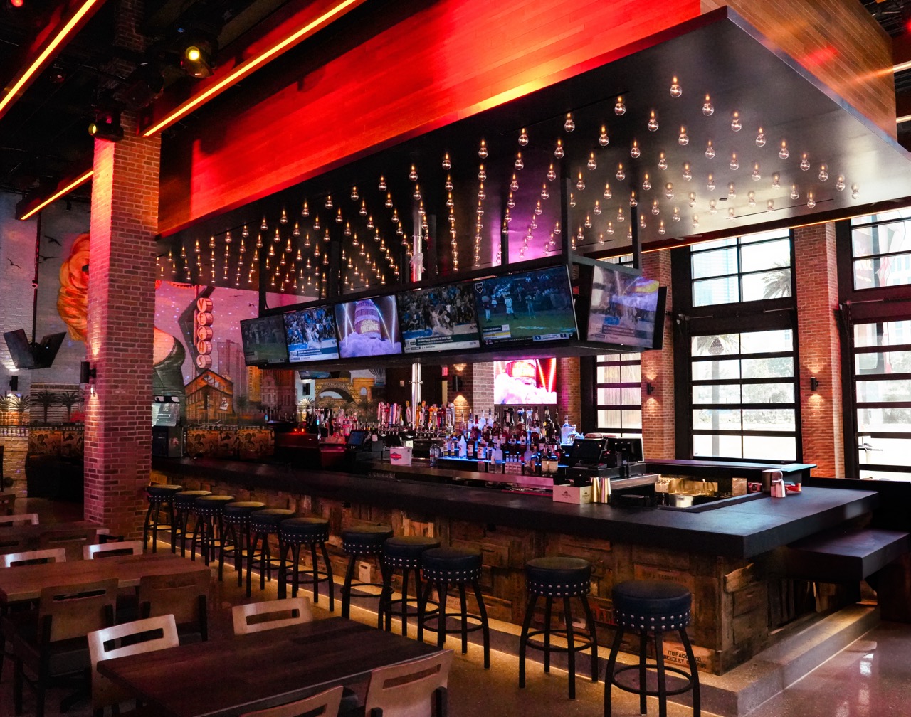 Modern bar with high ceilings, neon lights, and multiple televisions.