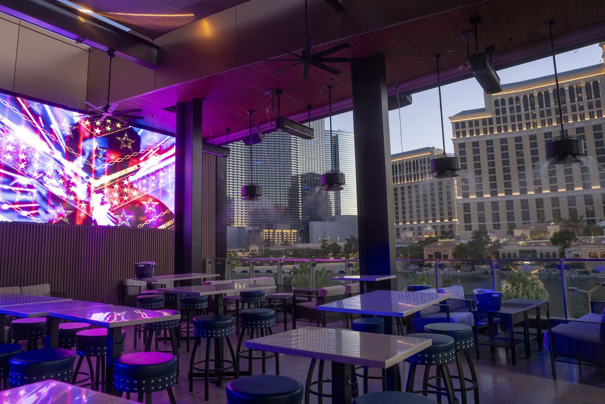 Rooftop bar in Las Vegas with modern seating and vibrant LED screen under twilight sky.
