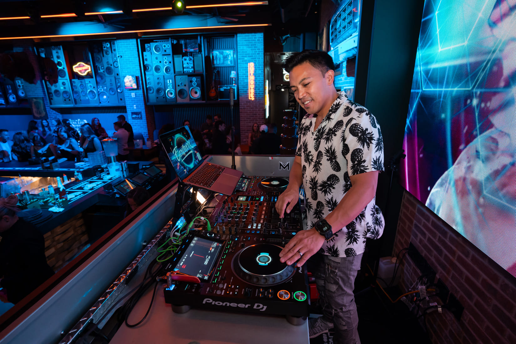 DJ performing at Bottled Blonde with a Pioneer DJ controller and crowd in background.