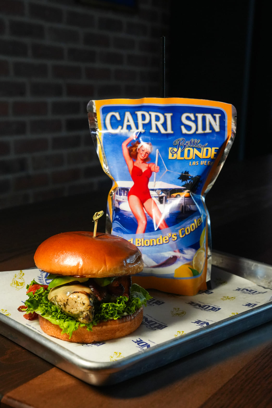 Chicken sandwich with lettuce and cheese next to Capri Sin drink pouch