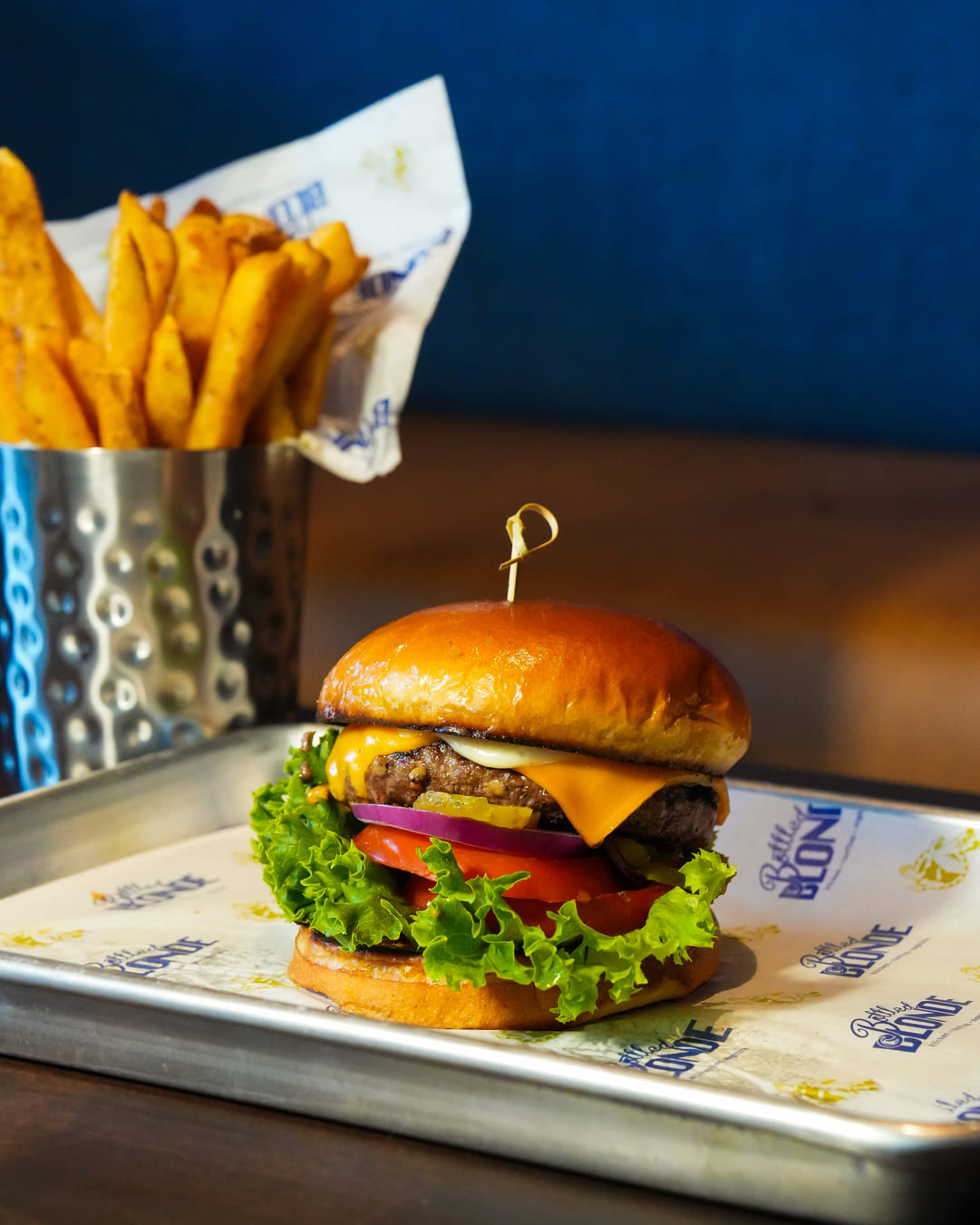 Cheeseburger with lettuce, tomato, and thick-cut fries in metal cup