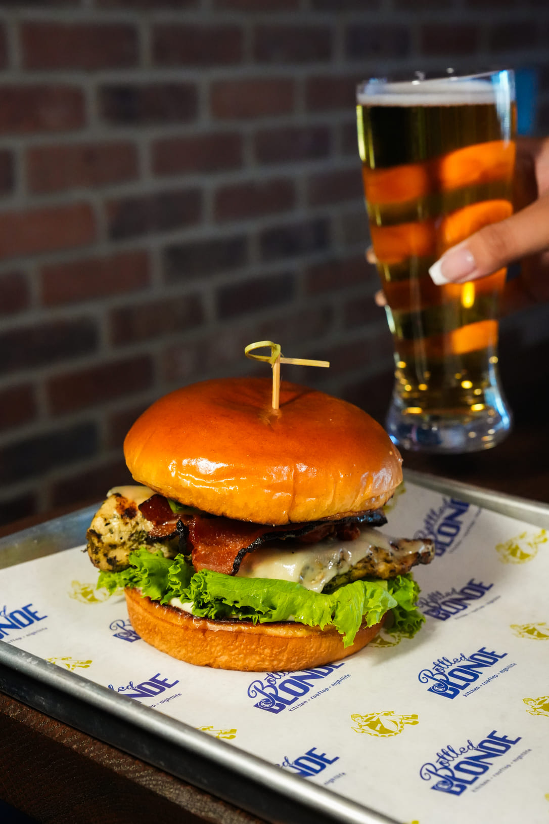 Grilled chicken sandwich with bacon and lettuce served with a glass of beer