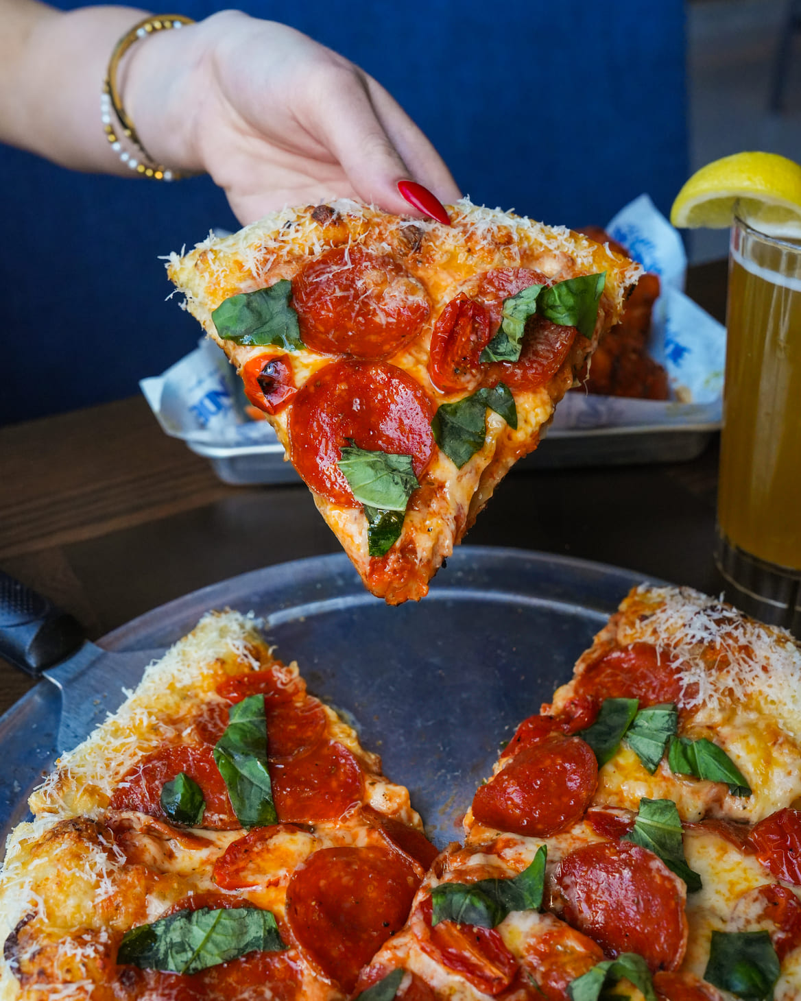 Hand holding a pepperoni pizza slice with fresh basil and cheese