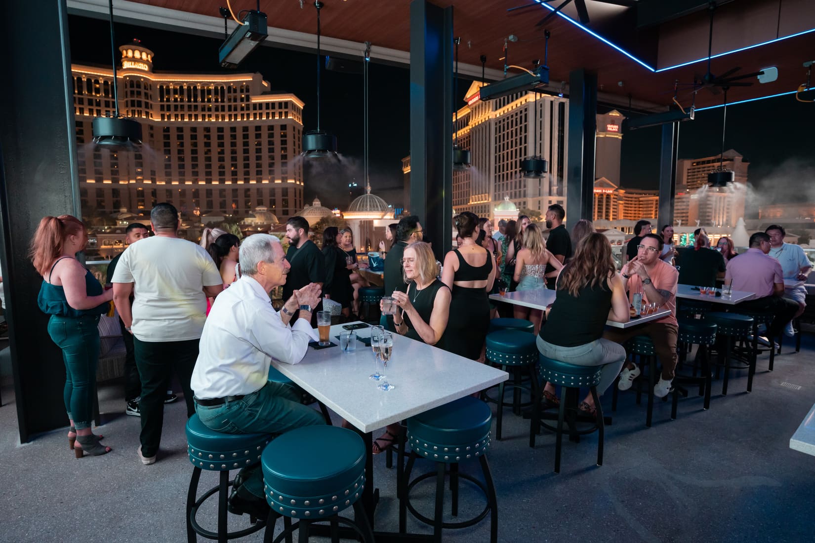 Crowded rooftop bar with views of the Las Vegas Strip at night.