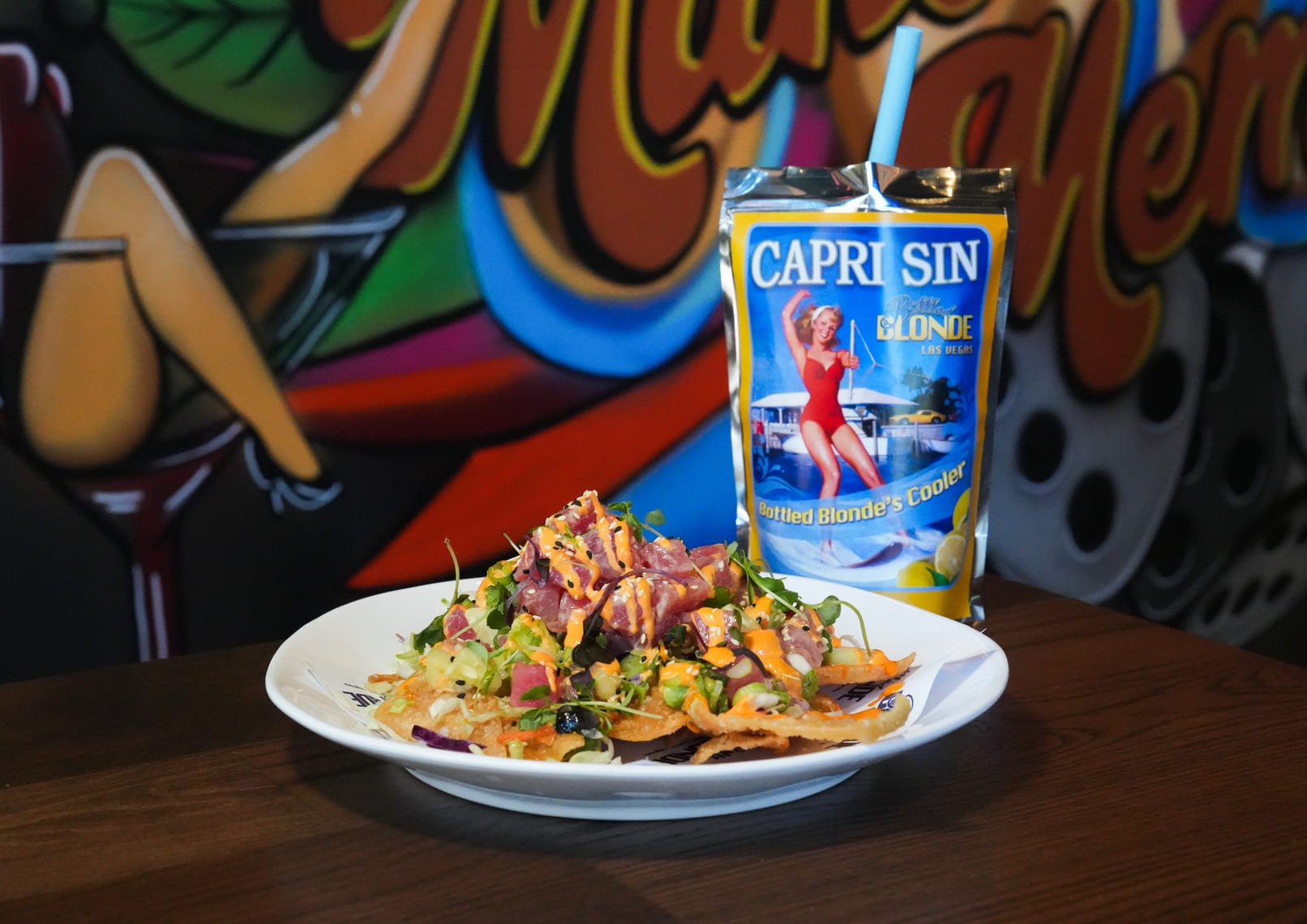 Tuna nachos on a white plate with a Capri-style drink pouch beside a colorful mural