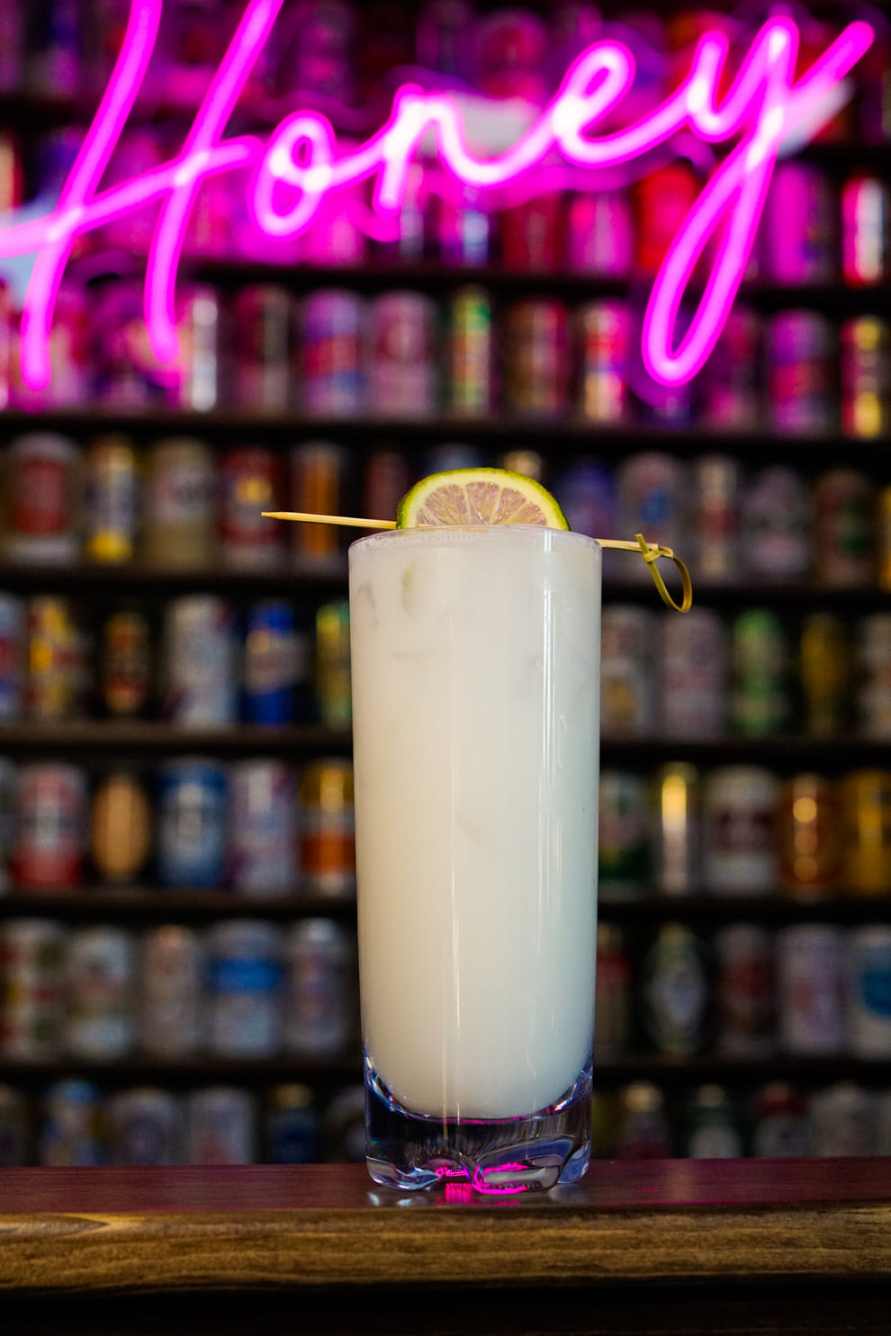 Creamy white cocktail with lime slice garnish in front of neon sign