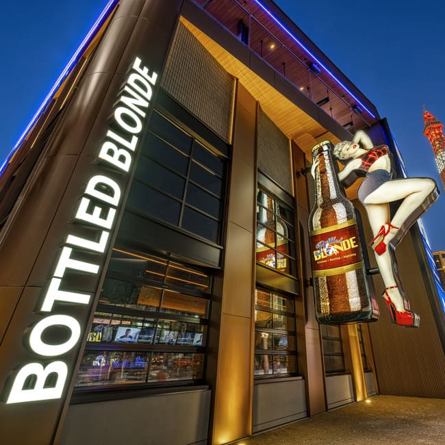 Exterior of Bottled Blonde Las Vegas with large illuminated sign, beer bottle, and pin-up style figure at night.