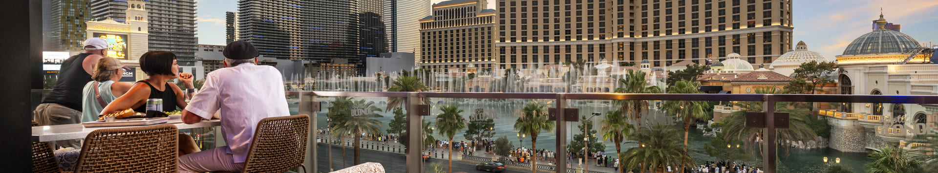 Rooftop seating at Bottled Blonde Las Vegas with guests dining and a view of the Bellagio and city skyline at sunset.