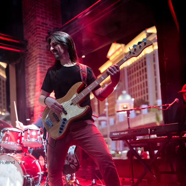 Bassist with long hair playing live on red-lit stage