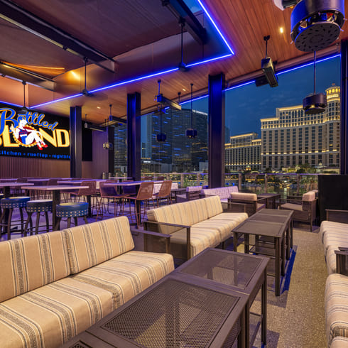 Outdoor rooftop lounge with striped sofas and tables overlooking the Las Vegas Strip at night.