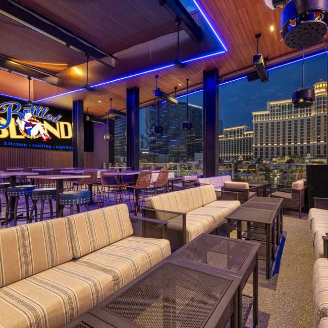 Outdoor rooftop lounge with striped sofas and tables overlooking the Las Vegas Strip at night.