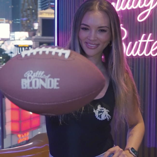 Woman smiling while holding a football with the Bottled Blonde logo.