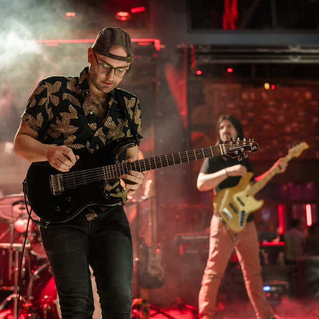 Guitarist performing live on stage with band under red lighting