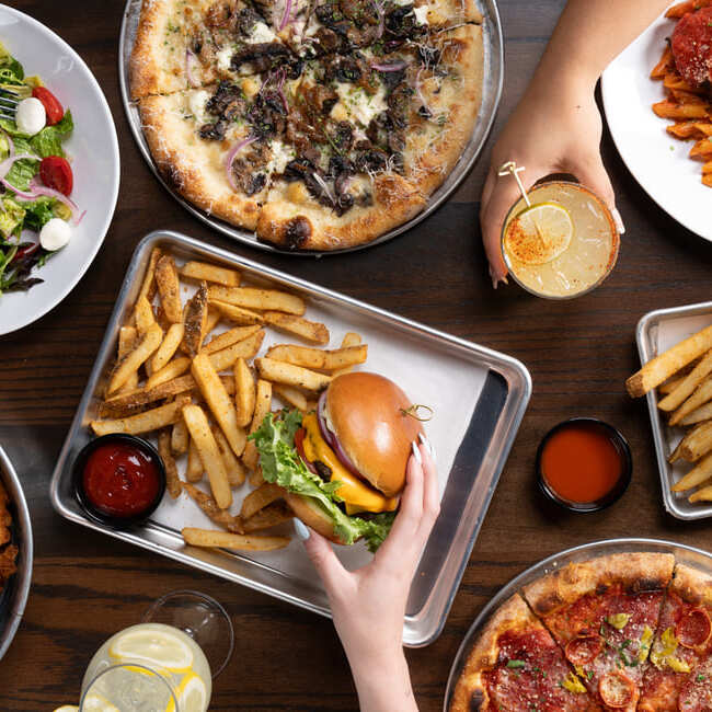 Overhead view of burgers, fries, pizza, and cocktails on a restaurant table