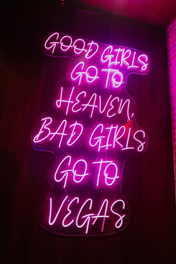 Pink neon sign reading “Good girls go to heaven, bad girls go to Vegas” on a nightclub wall.