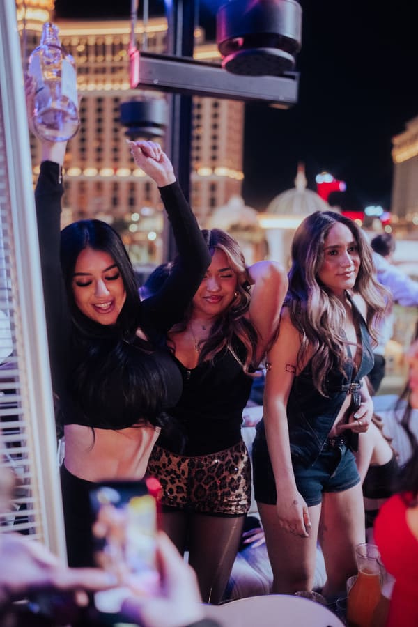 Three women dancing together at a rooftop nightclub with Las Vegas lights in the background.