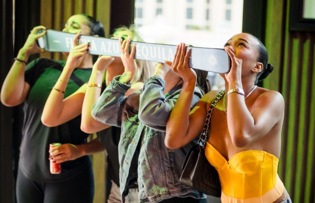 Group of friends taking tequila shots together using a shared shot dispenser in a bar